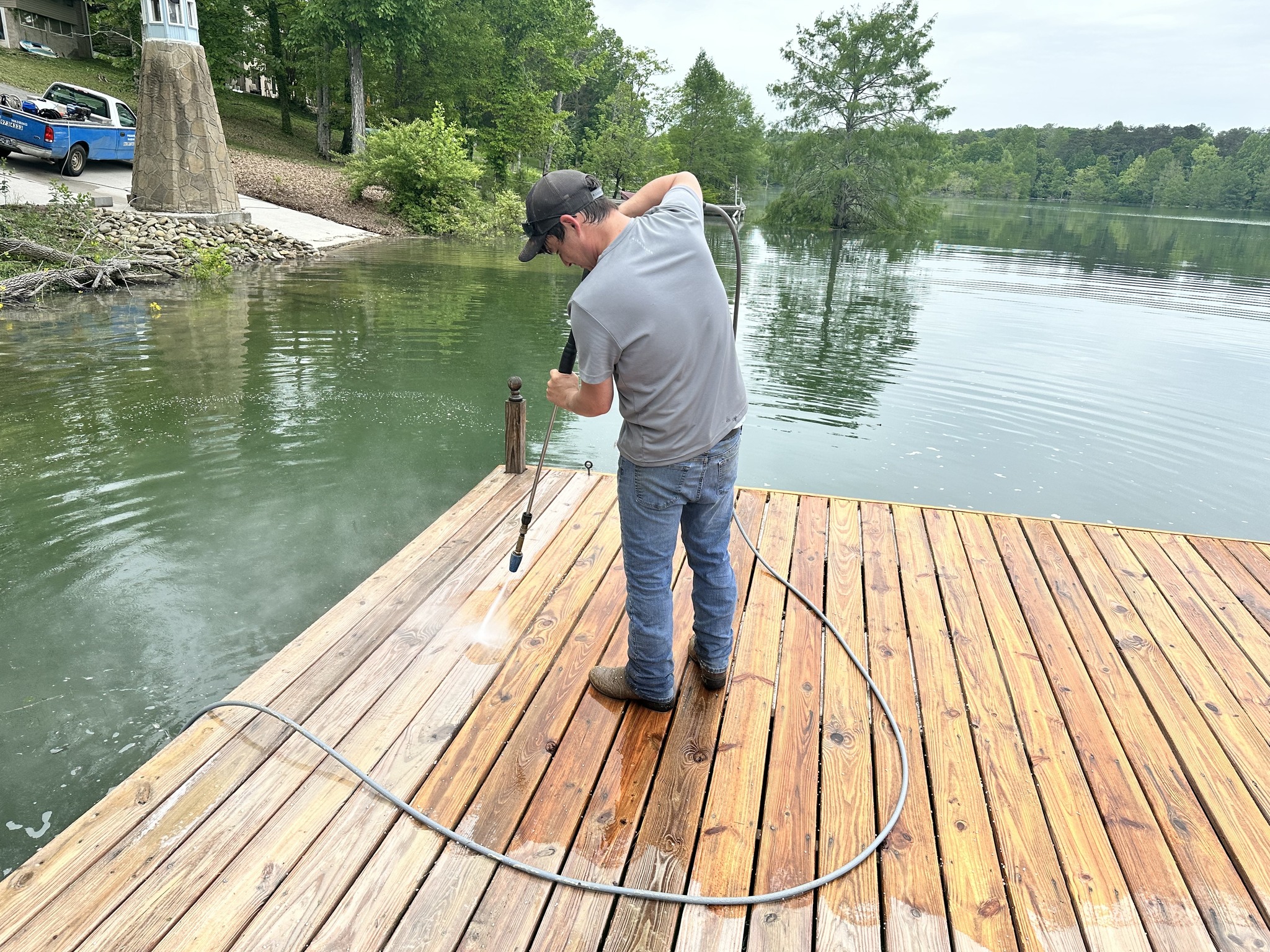 Blue Wave technician pressure washing a wooden dock on a lake